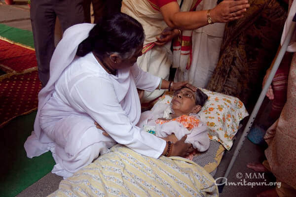 Amma consoling a bedridden on her way to the darshan hall