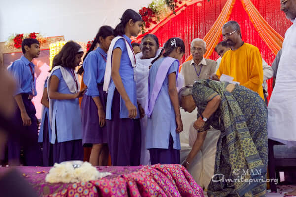 Sheila Dikshit while distributing Vidyamritam scholarships bend down to Amma's feet with each of the envelopes