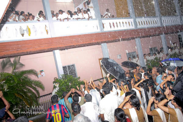 Devotees standing in the rain and cheering Amma watching from the balcony