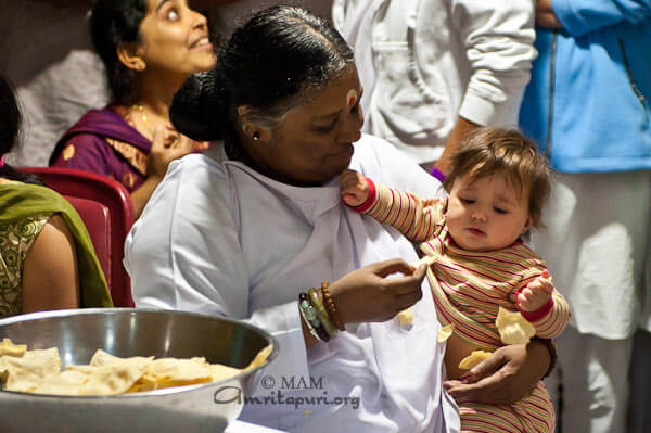 Amma feeding a baby with pappad at the retreat